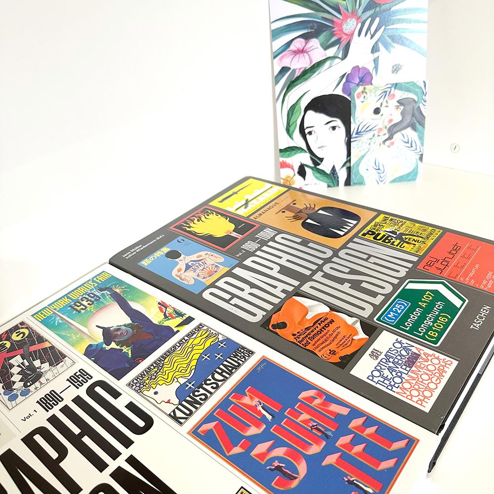Detailansicht des Studios. Zwei riesige Bücher vom Taschen Verlag mit dem Titel "Graphic Design". Im Hintergrund zwei Prints der spanischen Illustratorin Maria Hesse | DREIVIERTELNEUN Digital Design Studio